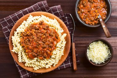 Homemade vegan bolognese sauce made with soy meat, fresh tomatoes, onion and garlic served on fusilli pasta on wooden plate, photographed overhead clipart