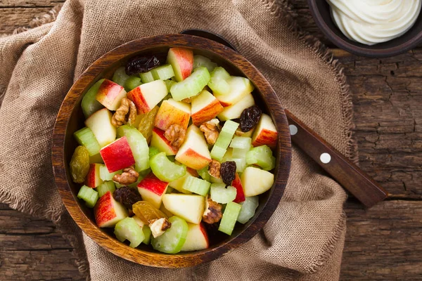 stock image Fresh Waldorf salad made of celery, apple, walnuts, sultanas and raisins in wooden bowl with mayonnaise on the side, photographed overhead