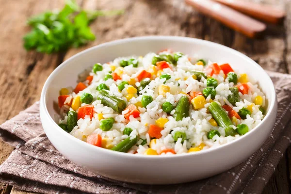 Cooked white rice mixed with colorful vegetables (onion, carrot, green peas, corn, green beans) in white bowl (Selective Focus, Focus in the middle of the dish)