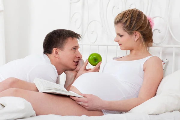Szczęśliwa Rodzina Ciąży Książki Jabłka Leży Łóżku Domu — Zdjęcie stockowe