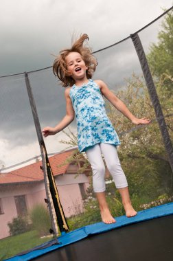 Small cute child jumping on trampoline - garden and family house in background clipart