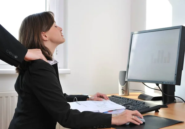 Business person (woman) on workplace with computer receiving neck massage from colleague (only hands visible)