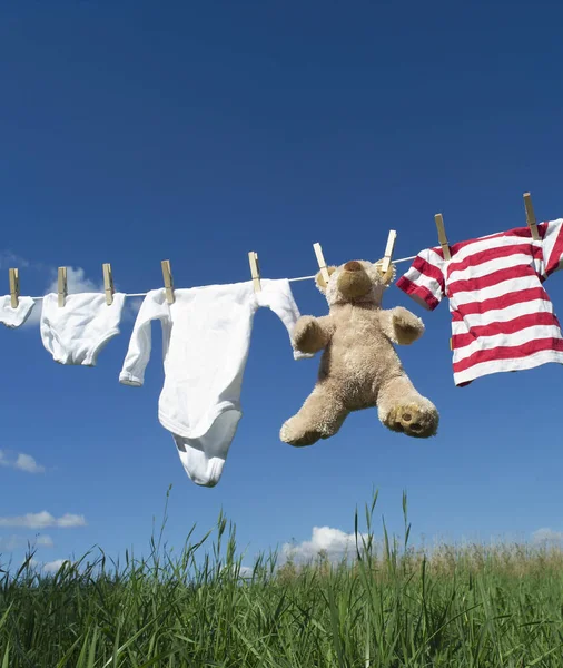 婴儿衣服和泰迪熊站在晾衣绳上朝向蓝天 — 图库照片