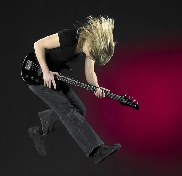 赤いバックの前で黒いベースのギターを弾いている女性が — ストック写真
