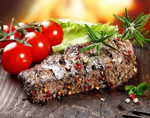 A grilled serving of succulent tender peppered steak garnished with lettuce, tomato and fresh rosemary herbs