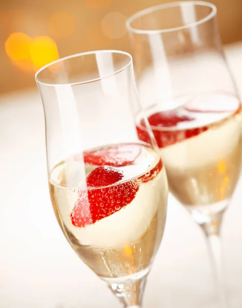 Closeup of stylish champagne flutes filled with chilled bubbly and a floating strawberry for celebrating a romantic evening together