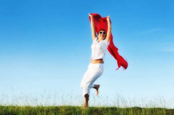 美しい女性の若くて健康な実行し 赤いスカーフと晴れた日で草原にジャンプ — ストック写真
