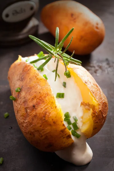 Sliced baked jacket potato cooked over a summer BBQ in foil with sour cream and chopped chives topped with rosemary for a delicious savory appetizer or vegetarian cuisine