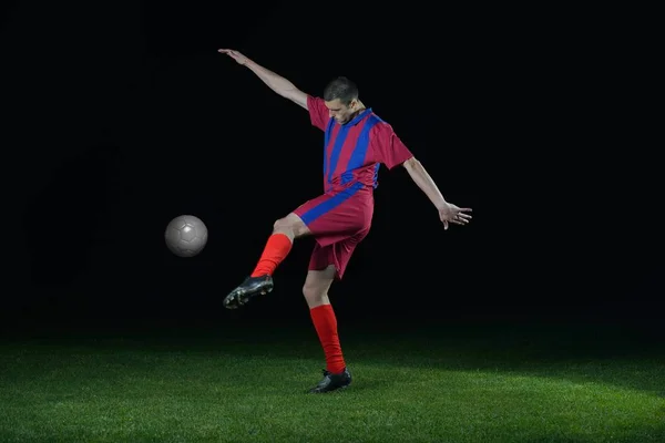 黒の背景上に分離されてサッカー スタジアムのフィールド上のボールをキックしているサッカー選手 — ストック写真