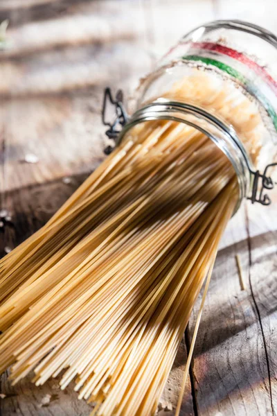 Healthy wholewheat Italian spaghetti pasta in a glass jar with the colors of the Italian national flag lying on its side on a rustic wooden surface in sunshine
