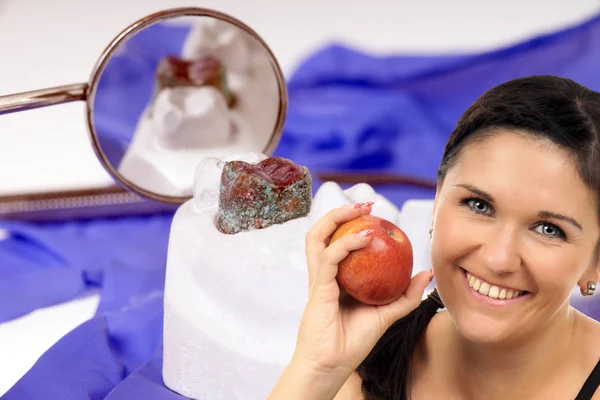 young woman with apple in front of a denture with dental mirror
