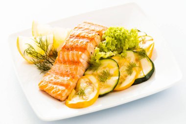 Salmon steak with sliced zucchini and courgette, lettuce and lemon garnished with fresh dill for a tasty seafood platter or appetizer clipart