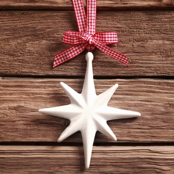 かなり赤と白のチェックリボンからぶら下がっ白いクリスマスの星の飾りと正方形の形式で素朴な質感の木に弓 — ストック写真