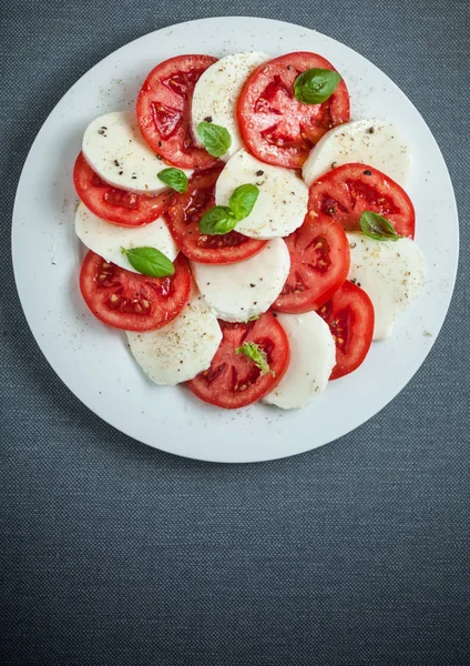 上から見たイタリアのカプレーゼサラダは トマトとモッツァレラチーズを新鮮なバジルで交互に色鮮やかな赤と白のパターンを示しています — ストック写真