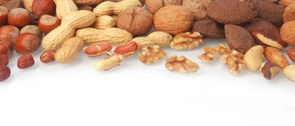 Mixed whole and shelled nuts in a horizontal banner including hazelnuts, brazil nuts, peanuts or groundnuts and walnuts on white with copyspace below