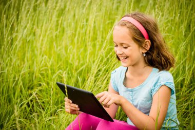 Smiling child working with tablet outdoor in nature clipart