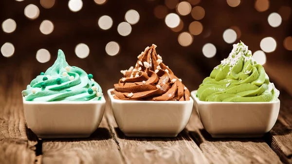 在一个灯火通明的派对上 一排五颜六色的三个不同的冻酸奶甜点 配上蓝色 棕色和绿色的果仁和糖珍珠 — 图库照片