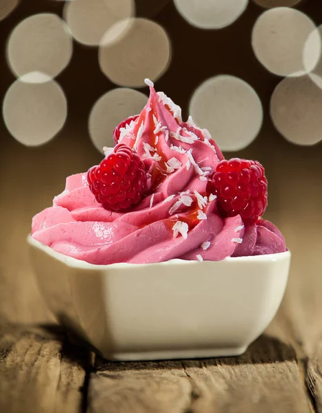 Tasty berry frozen yogurt drizzled with syrup and decorated with fresh raspberries for a colorful party dessert against a bokeh of twinkling lights