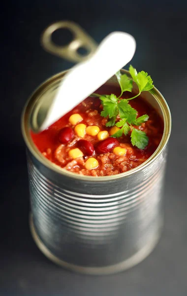 Opened can of wholesome vegetable soup with sweetcorn, kidney beans and lentils garnished with fresh parsley viewed from above