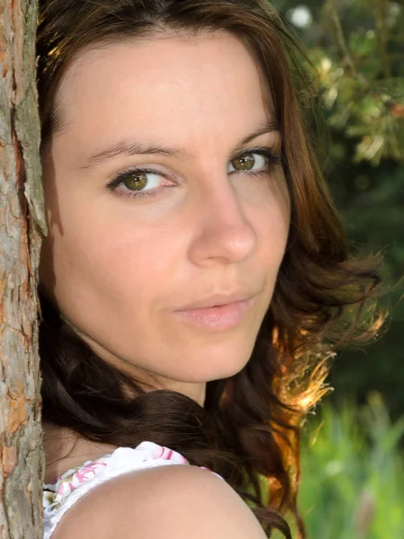 一个年轻 一头棕色头发 一双深绿色眼睛的女人靠着一棵树 脸上有温和的表情 眼神直率而紧张 她的头和肩膀都是她的画像 — 图库照片