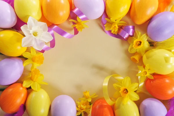 许多色彩艳丽的彩蛋和水仙花作为黄色桌布上的框架 — 图库照片