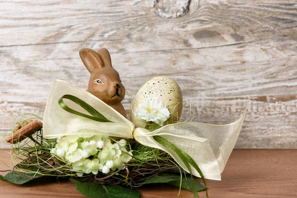 easter bunny with easter egg in nest in front of wood background as an easter greeting with free text space