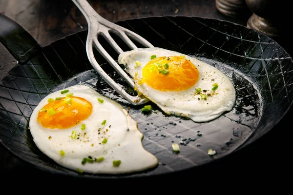 Two free range fried eggs seasoned with herbs in a skillet or pan ready to be served for a healthy breakfast