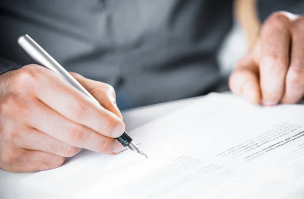 Close up of the hand of a man signing a contract or agreement with a fountain pen at the end of a block of text