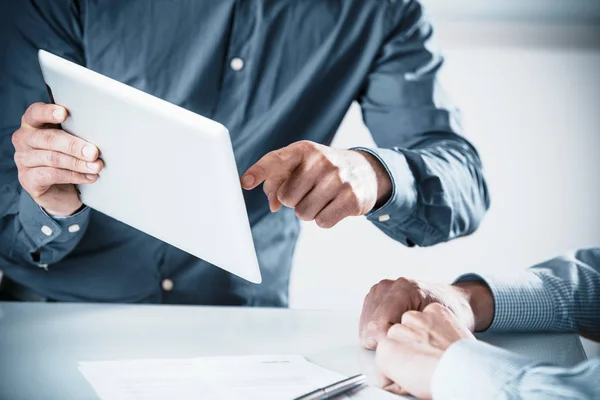 Two businessmen in a meeting discussing a projet on a tablet computer pointing to the screen, close up of their hands