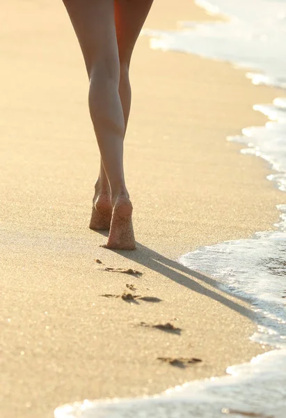 一个女人的腿在沙滩上行走留下的脚印的背光 — 图库照片