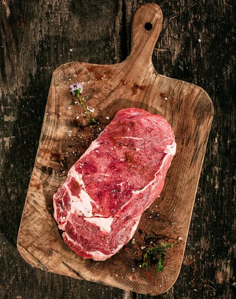 新鮮なハーブと塩で素朴な木のまな板に生の季節の霜降り牛リブアイステーキの高い角度ビュー — ストック写真