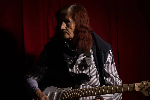 Funny elderly lady plays electric guitar in a dark room.