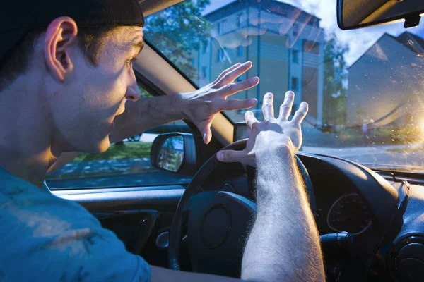 lateral wide-waist interior of a dazzled motorist (young man) hands protectively in front of him holding towards windshield with shocked look