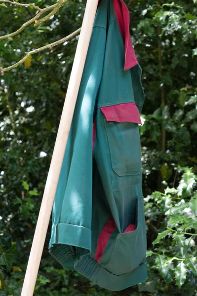 a green work jacket,hanging on a tool bar,in the park.