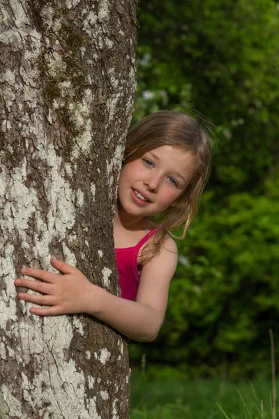 Ένα Ξανθό Κορίτσι Κοιτάζει Πίσω Από Ένα Δέντρο — Φωτογραφία Αρχείου