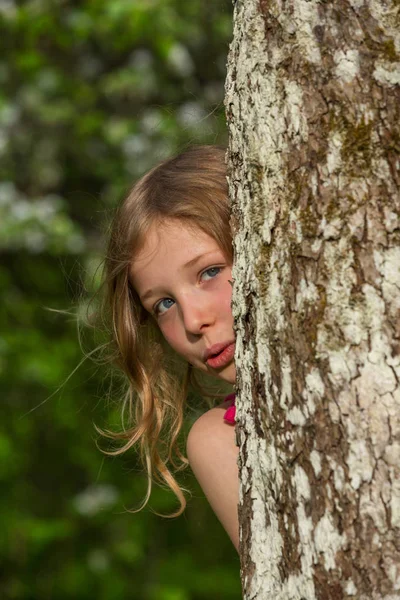 Ένα Ξανθό Κορίτσι Κοιτάζει Πίσω Από Ένα Δέντρο — Φωτογραφία Αρχείου