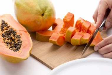Cutting a quarter of a papaya into six slices with a short kitchen knife. An entire fruit and a half are placed to the side. Juicy tangerine colored fruit pulp covered in lime green skin. Close up. clipart