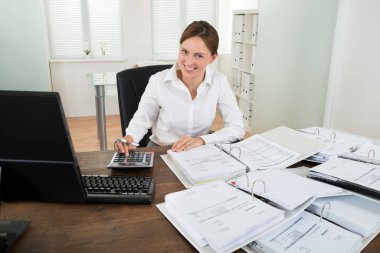 Happy Businesswoman Calculating Financial Data With Calculator At Desk clipart