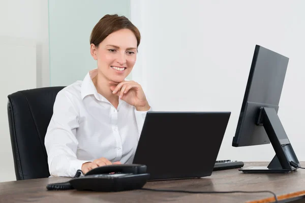 在办公桌前的笔记本电脑和台式计算机上工作的快乐的女商人 — 图库照片