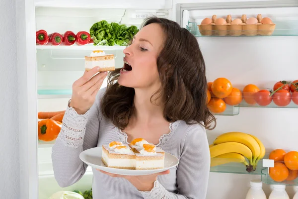 Mujer Joven Comiendo Rebanada Pastel Cerca Del Refrigerador Abierto — Foto de Stock