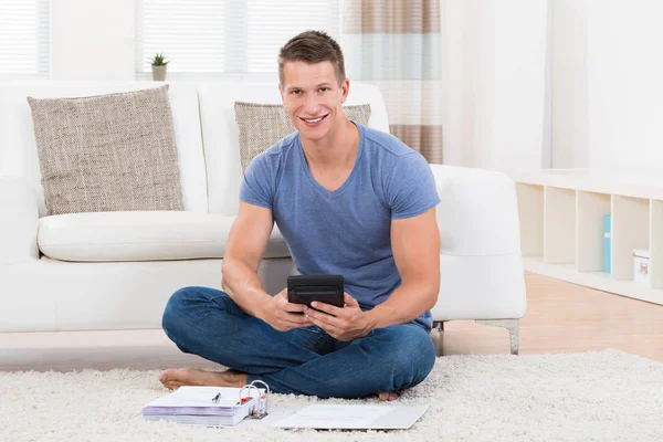 Junger Mann Sitzt Auf Teppich Und Berechnet Haushalt Mit Taschenrechner — Stockfoto
