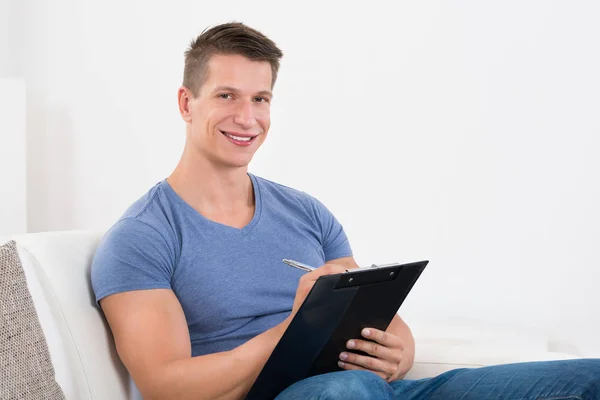 Happy Young Man Writing Clipboard While Sitting Sofa — Stock Photo, Image