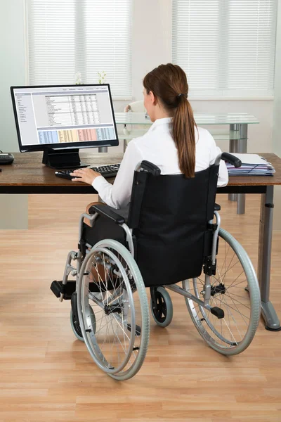 年轻的女建筑师坐在轮椅上看着办公室电脑上的蓝图 — 图库照片
