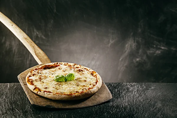 Steaming hot tasty margarita Italian pizza fresh from the pizza oven in a pizzeria served on a long handled wooden board with copyspace behind