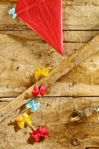 多色の装飾弓とカラフルな赤い素朴な手作りの凧は コピースペース オーバーヘッドビューと古い木製の板の背景に横たわって尾に結びました — ストック写真