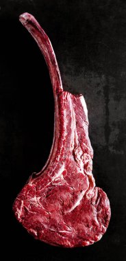 Lean raw tomahawk beef steak, so called for its shape on the bone, isolated on a black background in a close up overhead view clipart