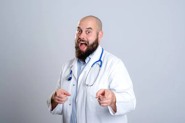 Beyaz Önlüklü Genç Sakallı Doktor Gülümsüyor Kameraya Işaret Ediyor — Stok fotoğraf