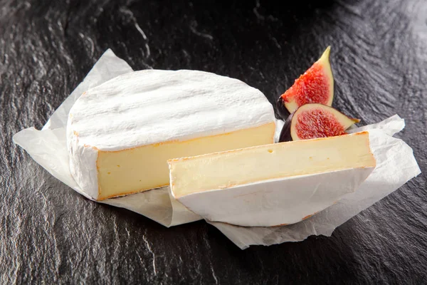 柔らかい熟したクリーミーなフランスのカンベールチーズのスライスラウンドダークな背景の上に砕いた白い紙ナプキンに本社ジューシーな熟した赤いイチジクを添えて — ストック写真