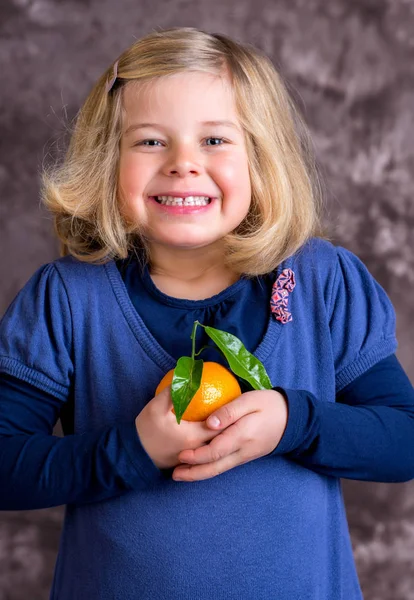 Klein Grappig Meisje Met Mandarijn Oranje Voorkant Van Bruine Achtergrond — Stockfoto