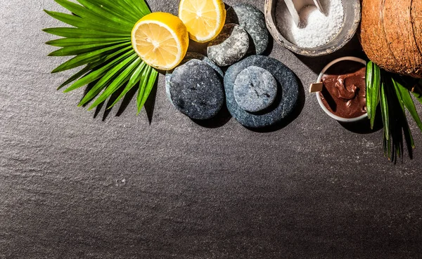 High Angle Background Image of Essential Spa Ingredients Arranged on Dark Gray Stone Surface with Copy Space - Leaves, Lemons, Smooth Stones and Mud Treatment